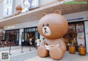 A woman posing in front of a giant teddy bear.