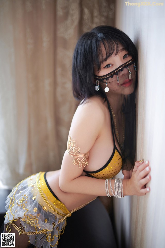 A woman in a yellow and black outfit leaning against a wall.