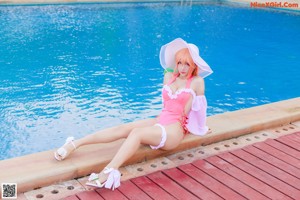 A woman in a pink bathing suit sitting by a pool.