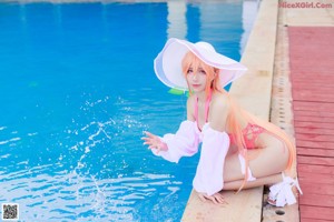 A woman in a pink swimsuit and a white hat by a pool.