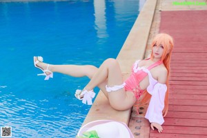 A woman in a pink bathing suit and a white hat by a pool.