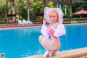 A woman in a pink bathing suit and a white hat by a pool.