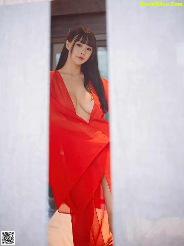 A woman in a red dress standing in front of a window.