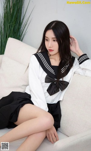 A woman in a school uniform sitting on a white couch.