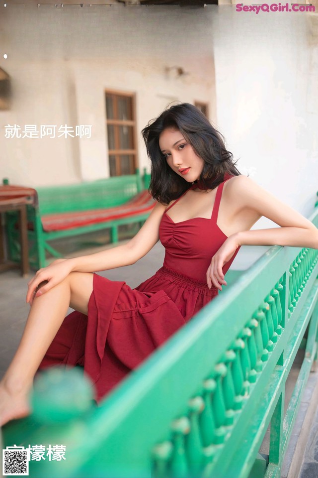 A woman in a red dress sitting on a green bench.