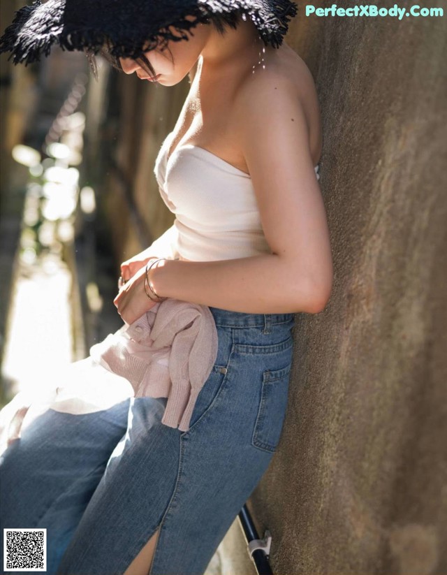 A woman leaning against a wall wearing a black hat.