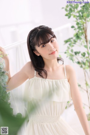 A woman sitting on a bed wearing a white dress.