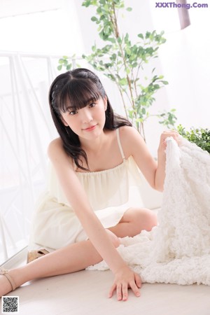 A woman in a white dress standing in front of a window.