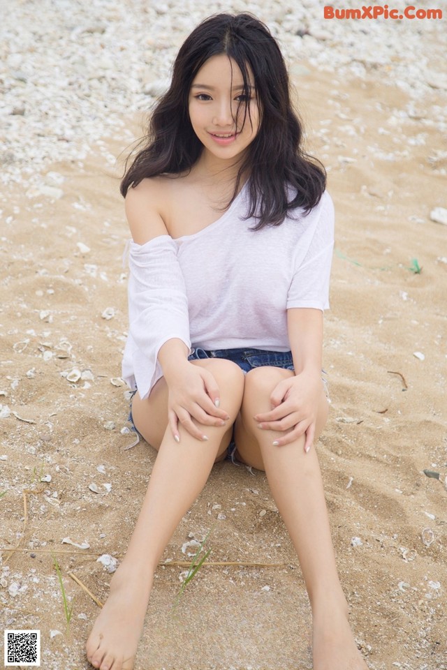 A woman sitting on a sandy beach with her legs crossed.