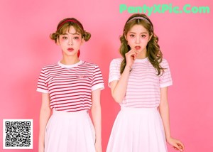 Two young women standing next to each other on a pink background.