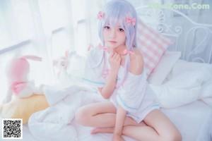 A girl in a pink dress sitting on a bed with a stuffed animal.