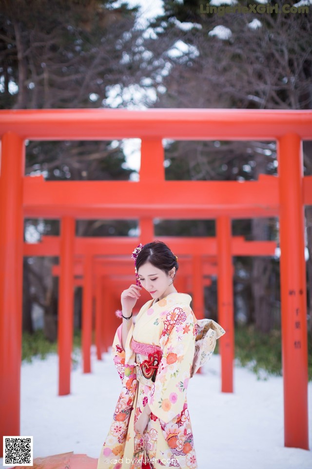 A woman in a kimono standing in front of a red torii gate.