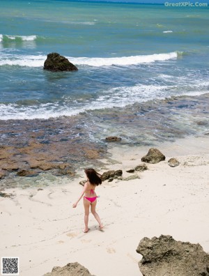 A woman in a pink bikini walking on a beach.