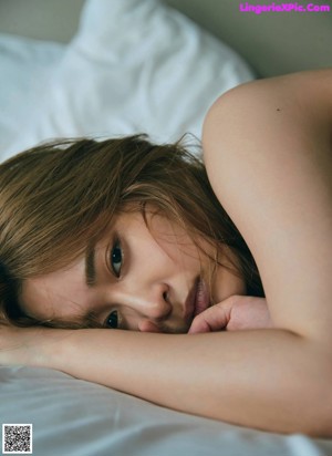 A naked woman sitting on top of a bed next to a wall.