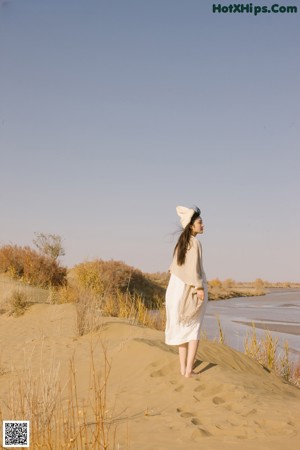 A woman in a white dress sitting on a sandy beach.