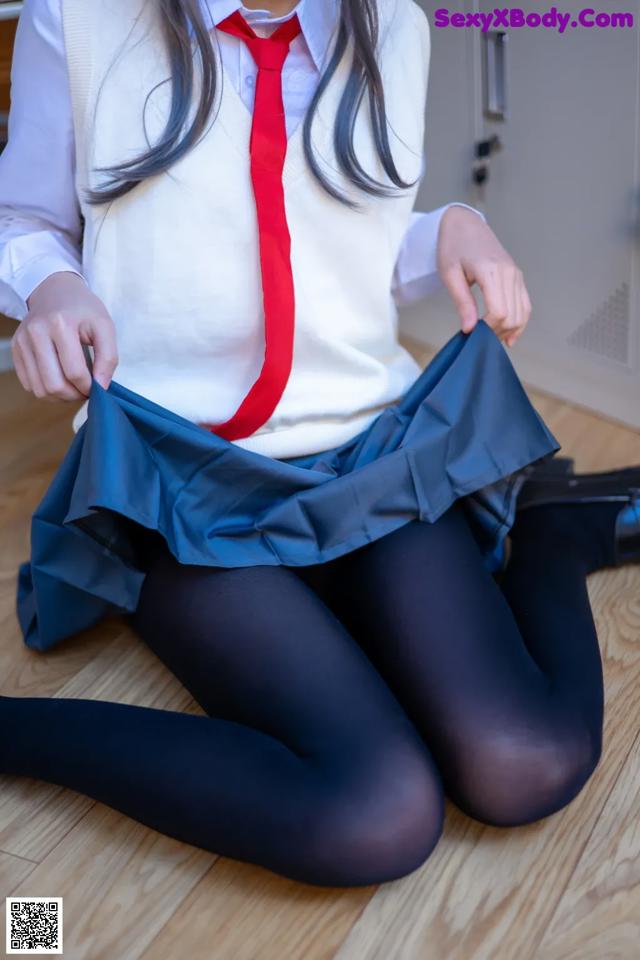 A woman in a school uniform is sitting on the floor.