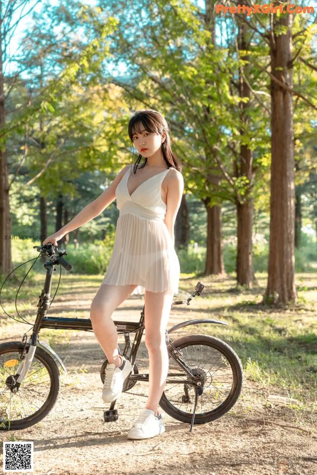 A woman in a white dress standing next to a bike.