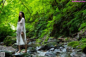 A naked woman standing in front of a waterfall.