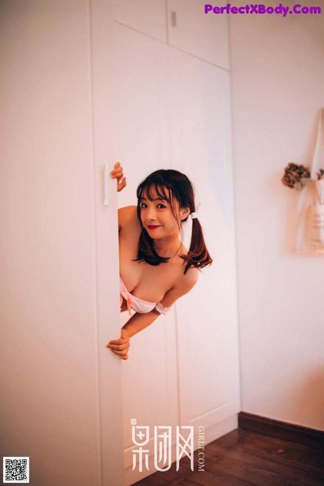 A woman in a pink bikini leaning against a white door.