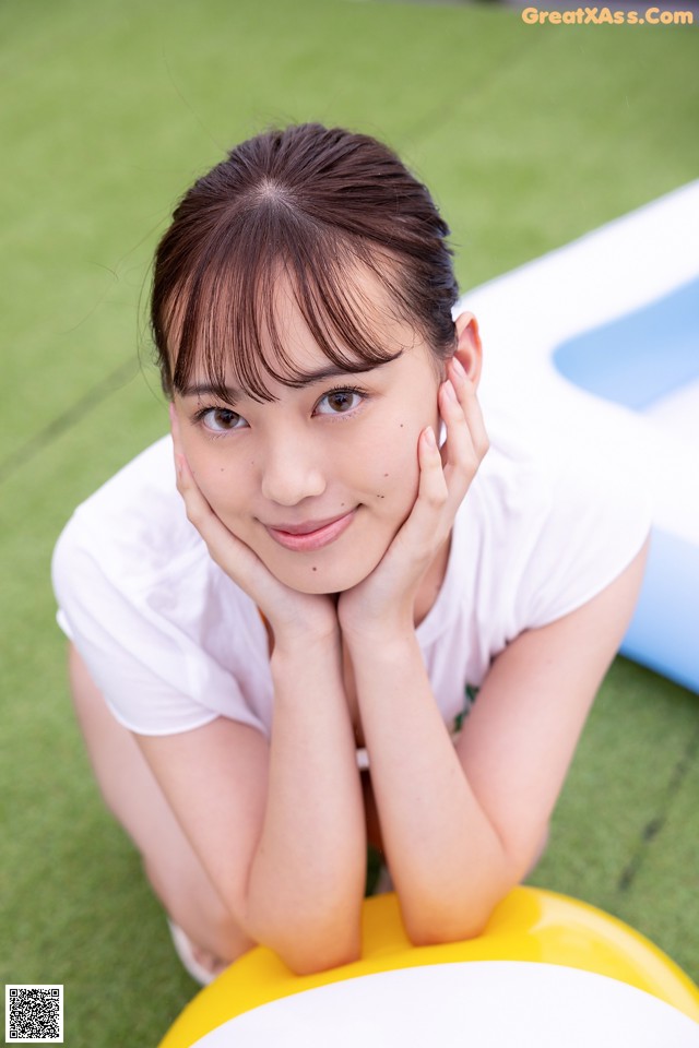 A young woman sitting on the ground with her hands on her face.