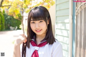 A young woman in a school uniform leaning against a wall.