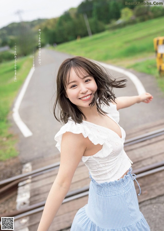 A woman in a white top and blue skirt posing on a train track.