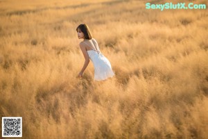 A woman in a white dress sitting in a field of tall grass.