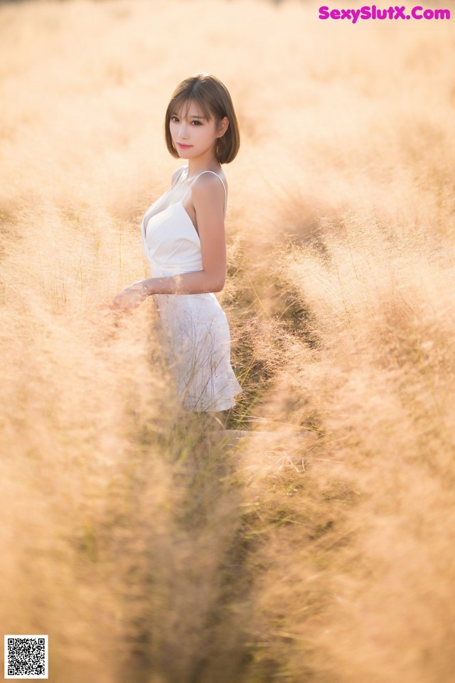 A woman in a white dress standing in tall grass.