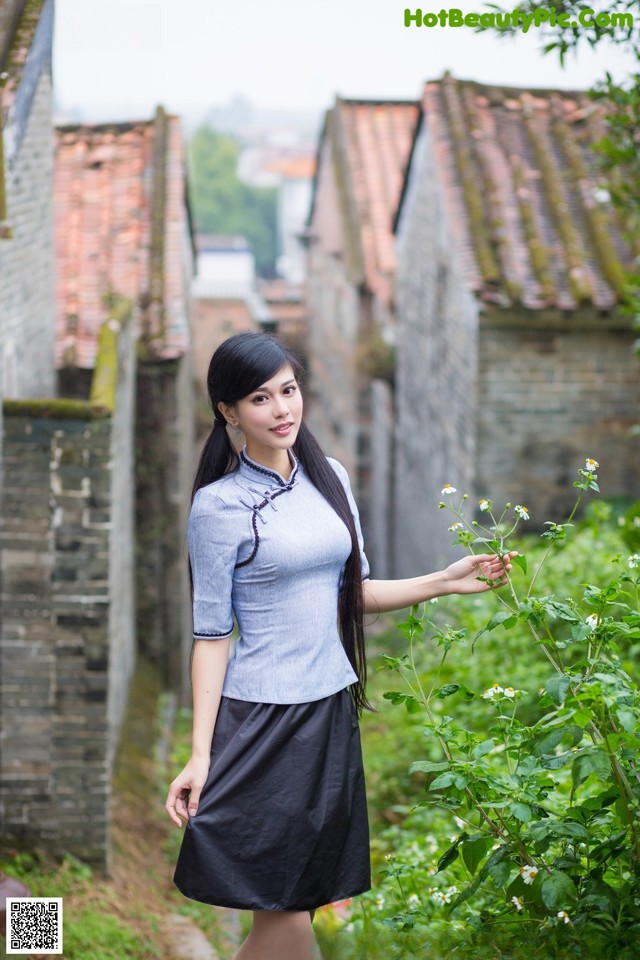 A woman in a blue shirt and black skirt standing in a garden.