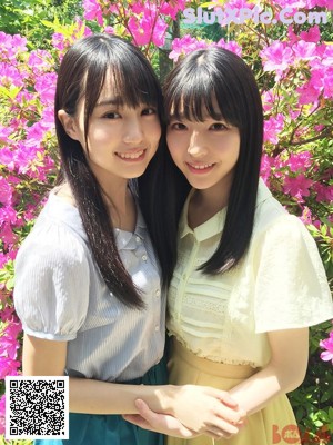 A couple of young women sitting next to each other near a fence.