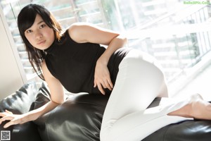 A woman sitting on a black couch holding a remote control.